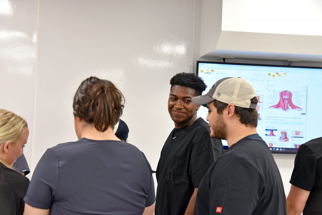 A group of students in anatomy lab standing in front of a SMART board.